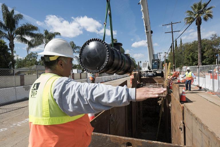 Water construction crew moving a water line using a crane.