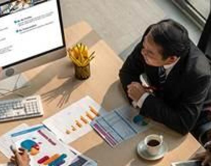 Two men and one women in office attire are sitting in an office conference room. Looking at a computer monitor. One of the men is pointing at the eRSP website page. The conference table is filled with business reports and charts.