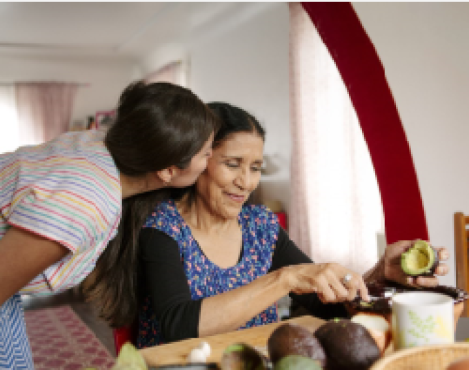 A young woman kisses the cheek of an older woman working in a kitchen.