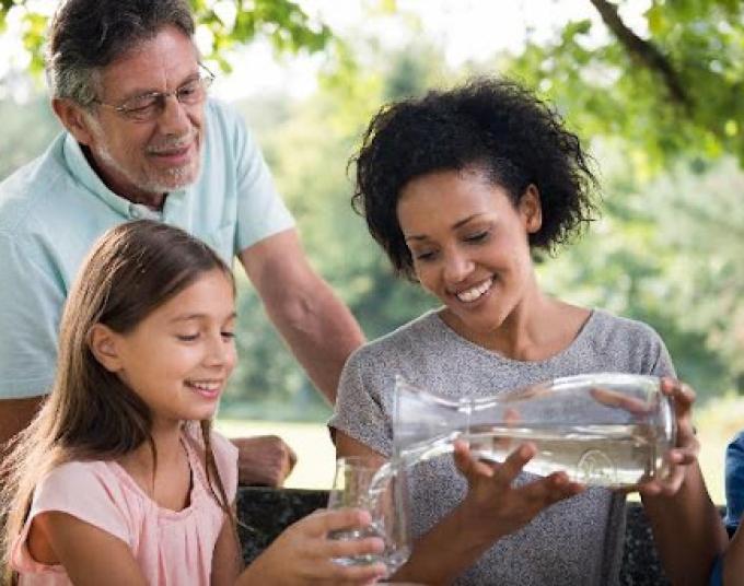 Family is outdoors and a smiling lady is serving water to a smiling kid.