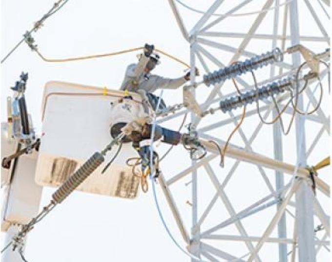 Lineworker high up in the air working on electrical wires.