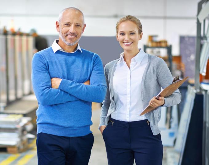 A businesswoman and businessman smile at the camera from inside their business’s warehouse.