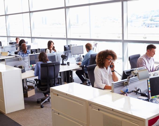 Workers sit at their desks in a busy office.