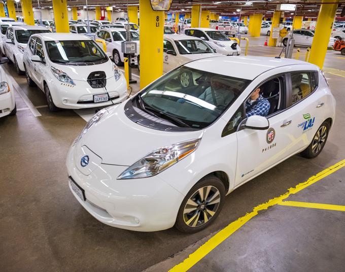 A white electric vehicle departing LADWP’s Fleet Services area. In the background, other electric vehicles are parked and charging.