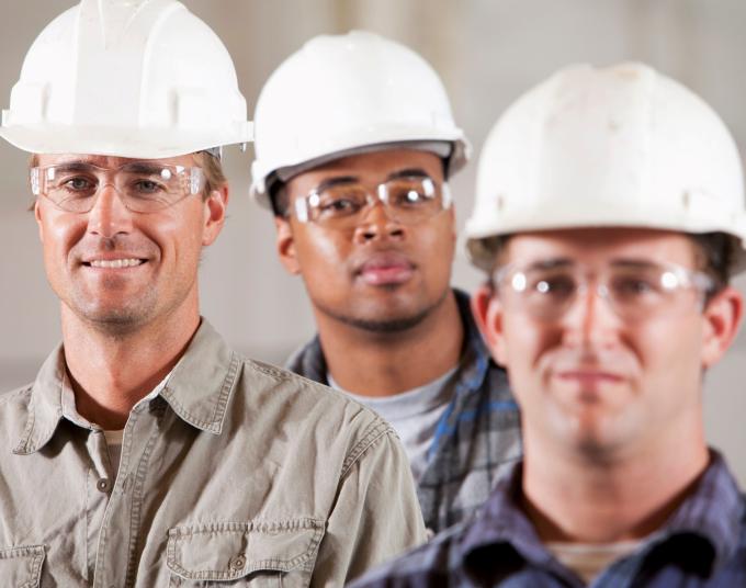 Three people in hard hats and protective eyewear smile at the camera.