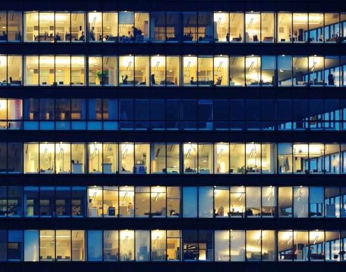 Some windows are illuminated and some are dark in an office building with large glass windows.