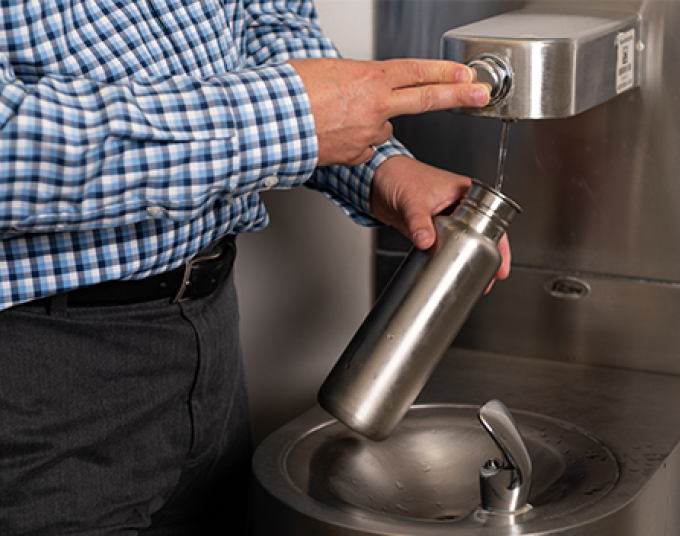 A person fills up a reusable water bottle at a hydration station.