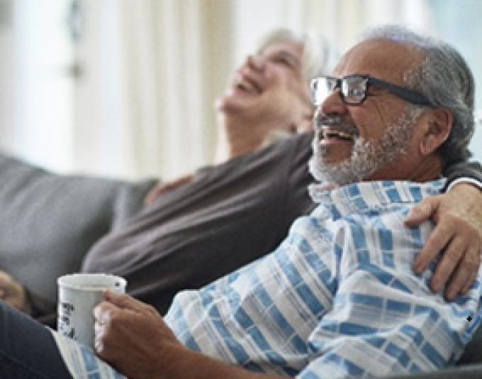 A smiling older couple sitting on a couch with arms around each other.