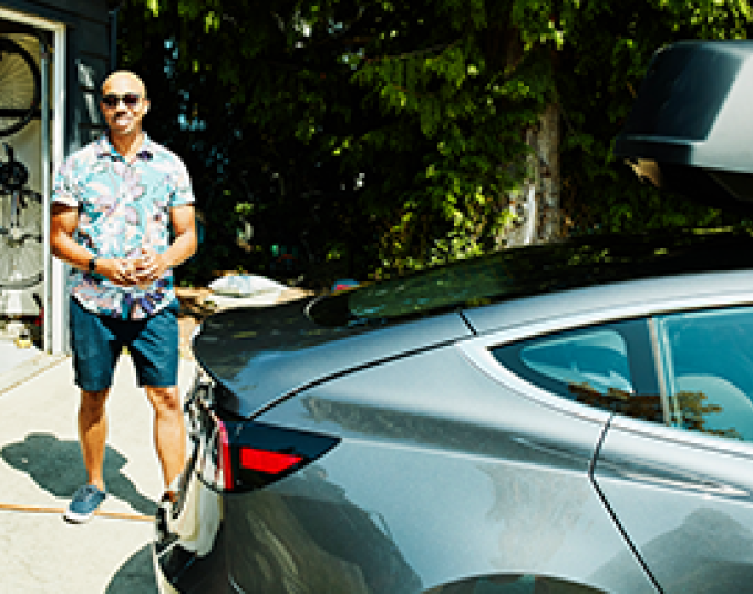 Man standing next to a gray electric vehicle that is charging. 