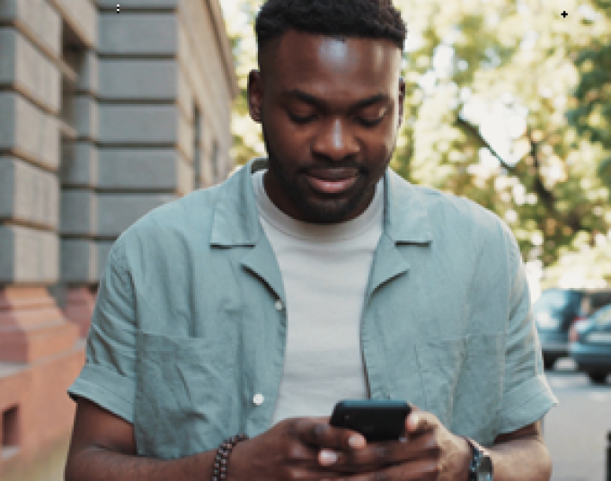 Outside by a building, a man is standing and looking down at his phone in his hands.