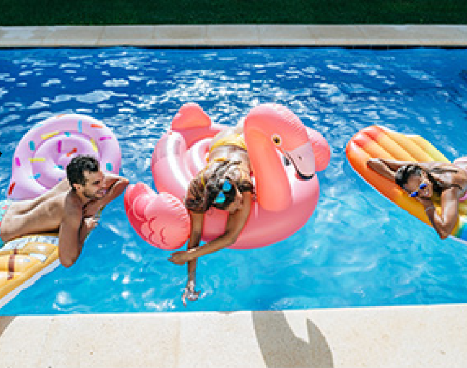 Three smiling adults in a pool on bright-colored pool floats.