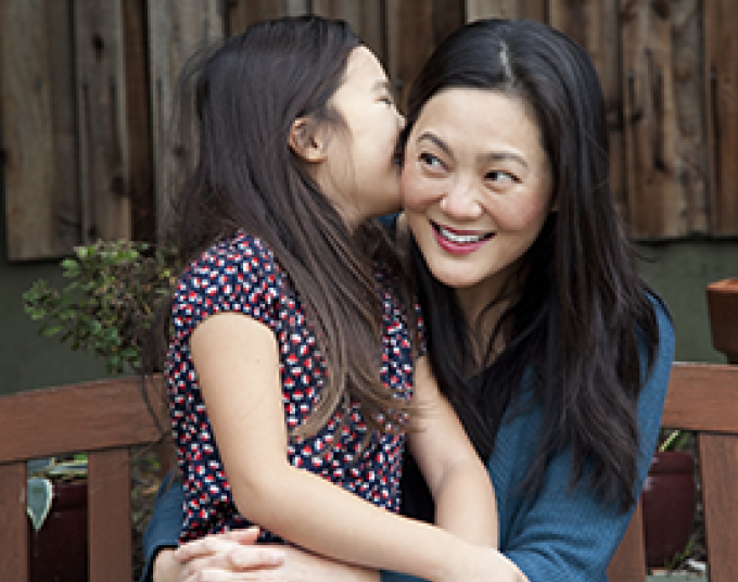 A child kisses a woman on the cheek while they sit on a wood bench.