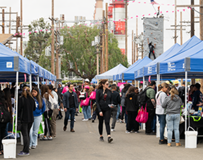 People outside walking down an aisle between two rows of booths with blue LADWP canopies over each one.