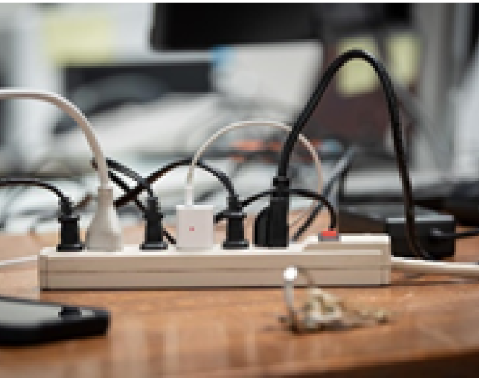 Power strip placed on a table with six power chords plugged into it. A cell phone is being charged.