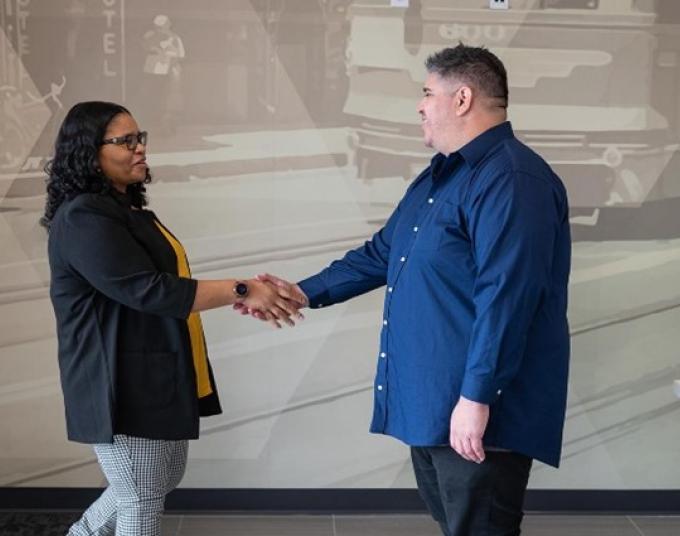 Smiling lady and man are indoors greeting each other by shaking hands.