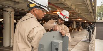 Photo shows Workers in hard hats perform maintenance and install an electric vehicle charging station.