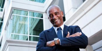 Smiling businessman stands outside a commercial building.