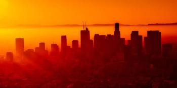 A city skyline is silhouetted against a red sky.