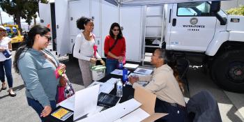 Three women talk to an LADWP staffmember who sits at an event table. An LADWP trailer is in the background. 